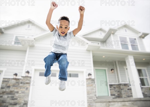 Mixed race boy jumping for joy in driveway