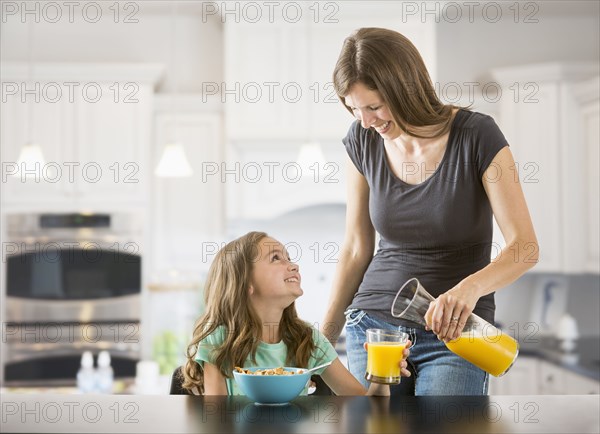 Caucasian mother pouring juice for daughter in kitchen
