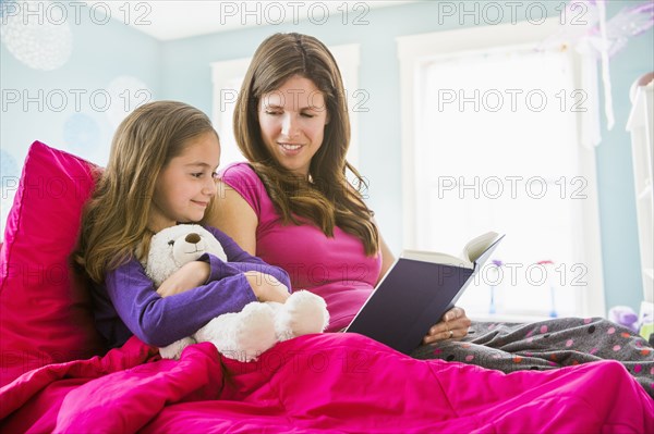 Caucasian mother and daughter reading in bed