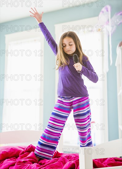 Caucasian girl singing into hairbrush on bed