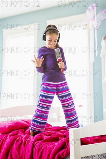 Caucasian girl singing into hairbrush on bed