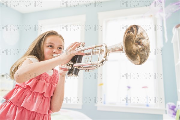 Caucasian girl playing trumpet in bedroom