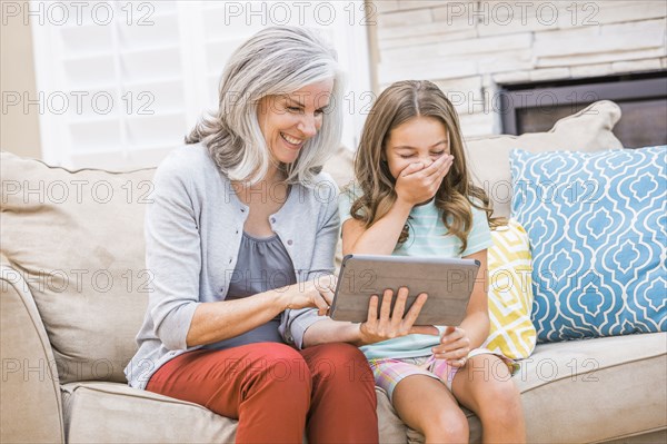 Caucasian grandmother and granddaughter using digital tablet on sofa