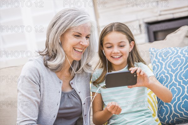 Caucasian grandmother and granddaughter listening to cell phone
