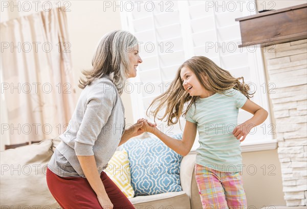 Caucasian grandmother and granddaughter dancing in living room