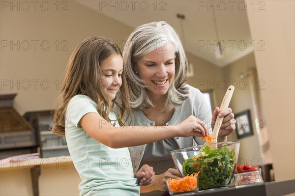 Caucasian grandmother and granddaughter making salad in kitchen