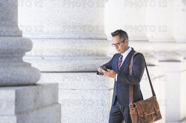 Mixed race businessman using cell phone under columns