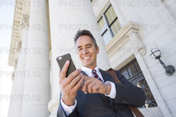 Mixed race businessman using cell phone outside courthouse
