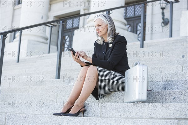 Caucasian businesswoman using cell phone on courthouse steps
