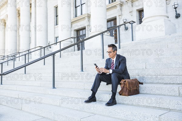 Mixed race businessman using cell phone on courthouse steps