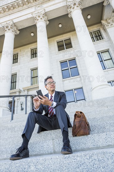 Mixed race businessman using cell phone on courthouse steps