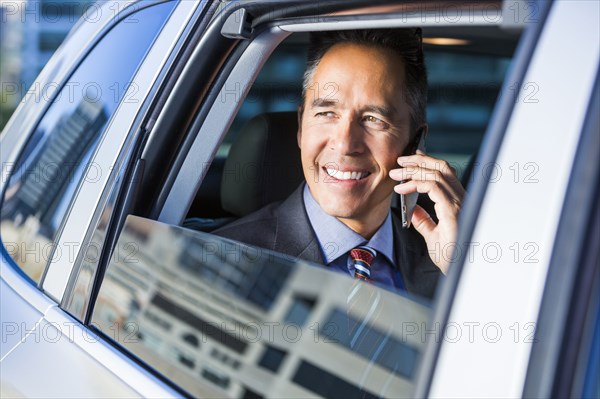 Mixed race businessman talking on cell phone in car