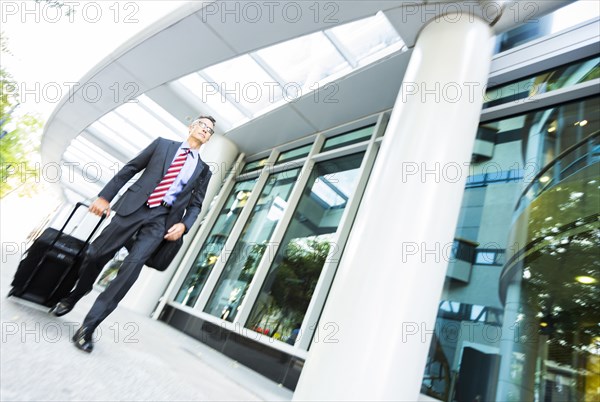 Mixed race businessman rolling luggage in office