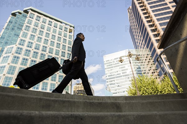 Mixed race businessman rolling luggage outdoors
