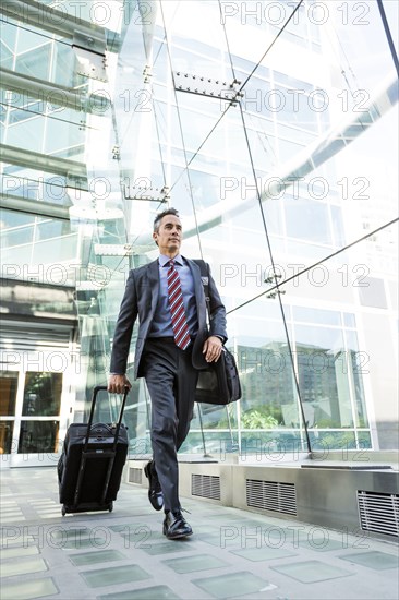 Mixed race businessman rolling luggage outdoors