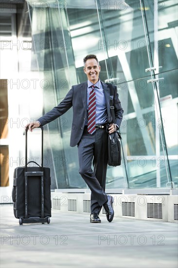 Mixed race businessman rolling luggage outdoors