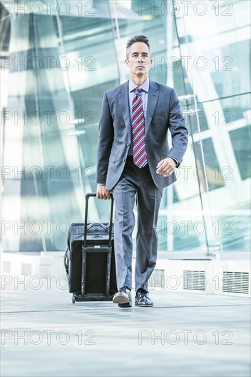 Mixed race businessman rolling luggage outdoors