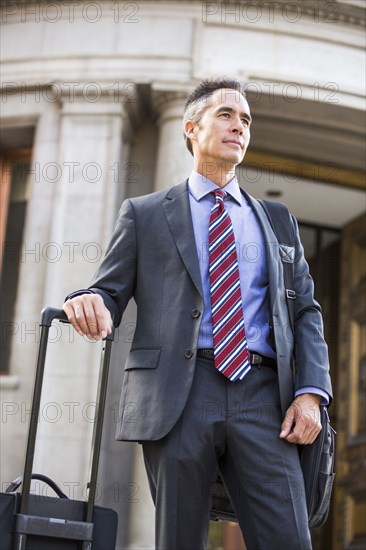 Mixed race businessman rolling luggage outdoors