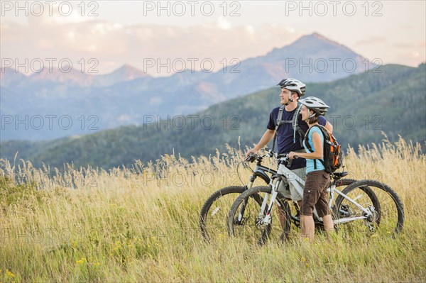 Caucasian couple riding mountain bikes in field
