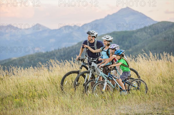 Caucasian family riding mountain bikes in field