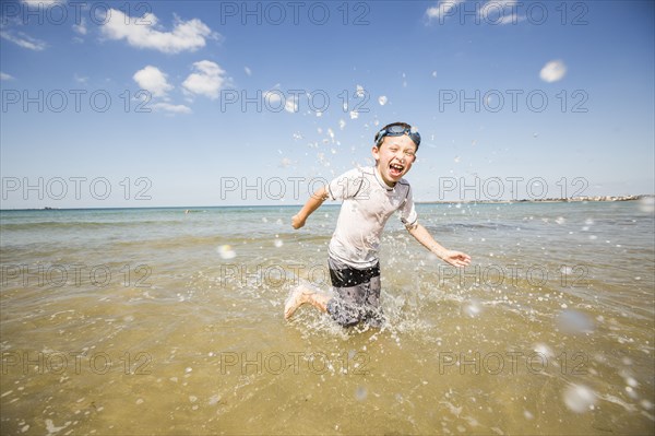 Caucasian boy splashing in waves on beach