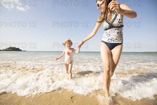 Caucasian mother and daughter playing in waves on beach