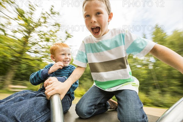 Caucasian boys playing on merry-go-round