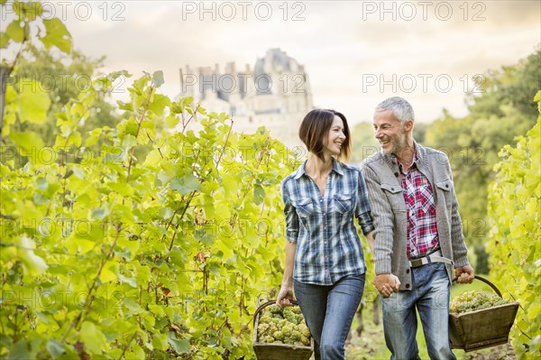 Caucasian farmers carrying grapes in vineyard