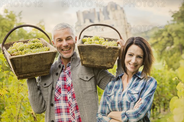 Caucasian farmers carrying grapes in vineyard