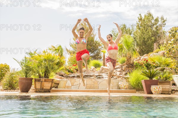 Caucasian women jumping into swimming pool