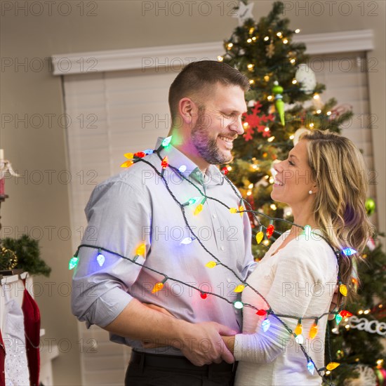 Caucasian couple wrapped in Christmas lights