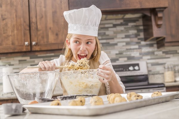 Caucasian girl tasting cookie dough in kitchen