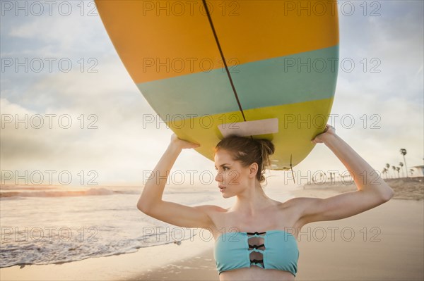 Caucasian woman carrying surfboard on beach