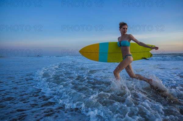 Caucasian woman carrying surfboard on beach