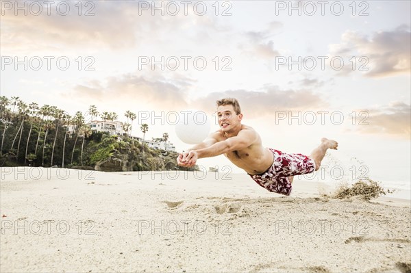 Caucasian man diving for volleyball on beach