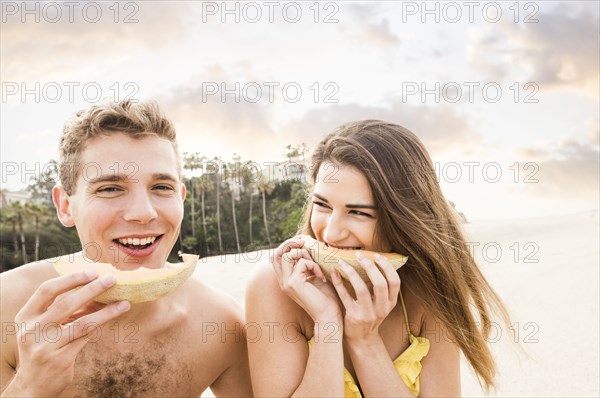 Caucasian couple eating fruit on beach