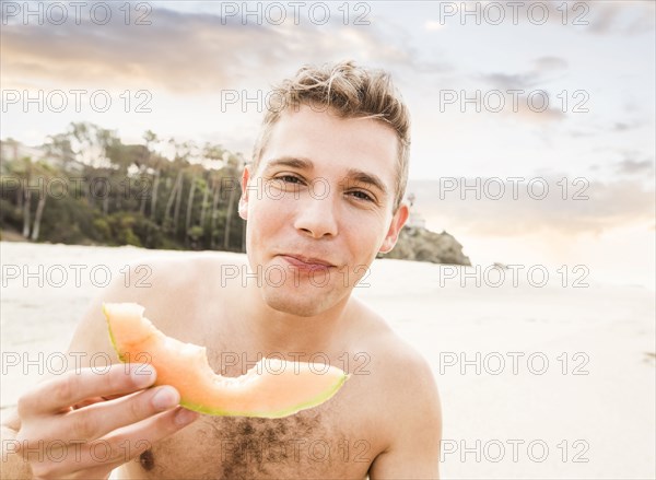 Caucasian man eating fruit on beach