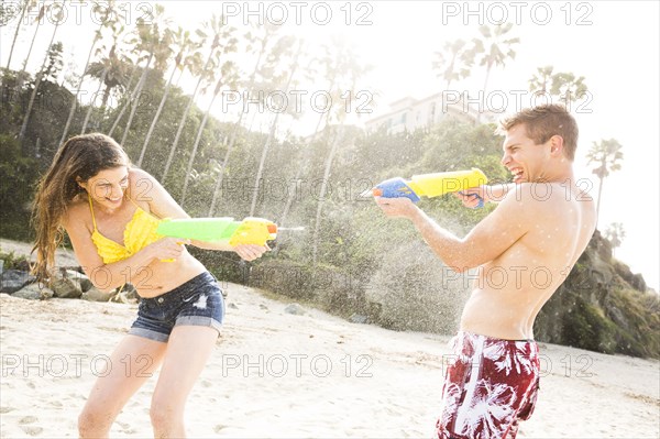 Caucasian couple playing with squirt guns on beach