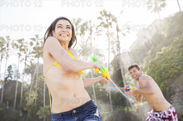 Caucasian couple playing with squirt guns on beach