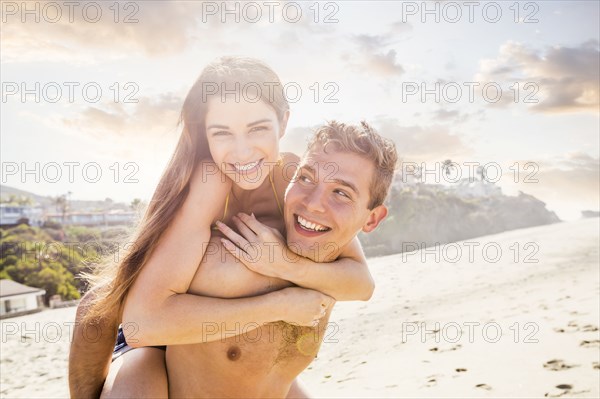 Caucasian man carrying girlfriend on beach