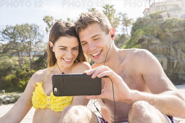 Caucasian couple using cell phone on beach