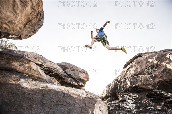 Caucasian teenage boy leaping over boulders