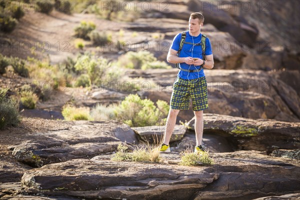 Caucasian teenage boy using cell phone on rock formation