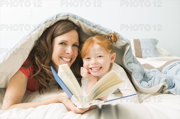 Caucasian mother and daughter reading book in bed