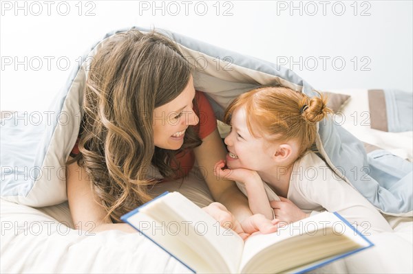 Caucasian mother and daughter reading book in bed