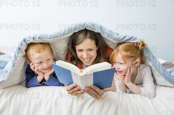 Caucasian mother and children reading book in bed