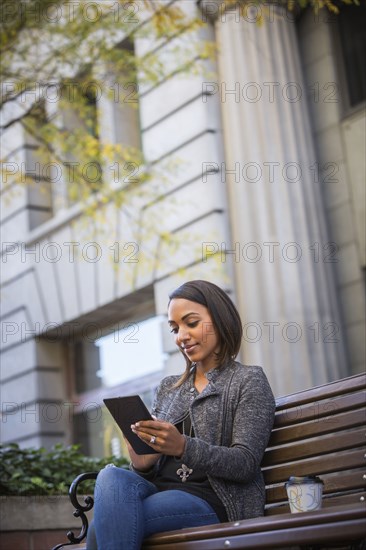 Indian woman sitting on city bench using digital tablet