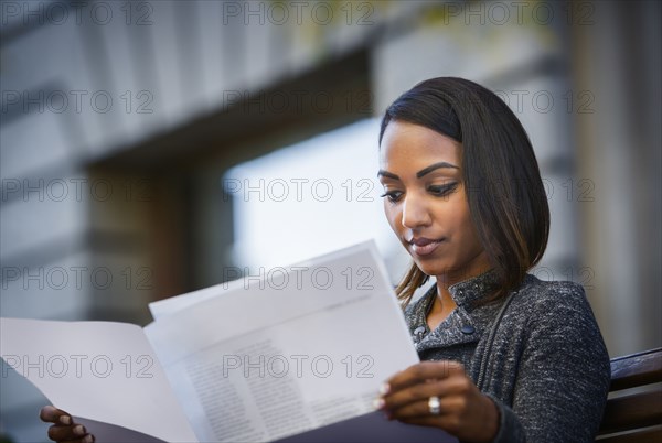 Indian woman sitting on city bench reading paperwork