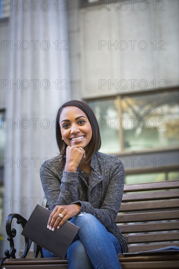 Indian woman sitting on city bench holding booklet
