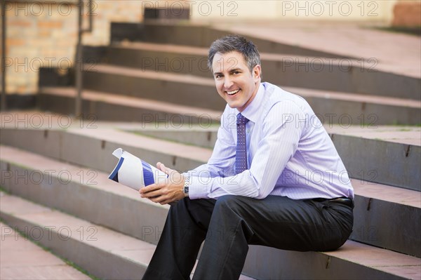 Caucasian businessman sitting on staircase holding paperwork